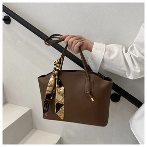 Brown leather tote bag detail with decorative floral silk scarf on a handle