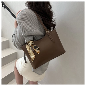 Detail of dark brown leather tote bag featuring a decorative scarf and fine stitching