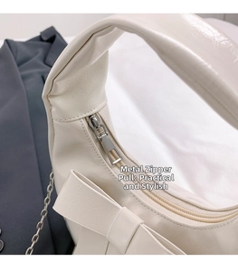 Detail of silver zipper and bow decoration on cream leather crossbody bag
