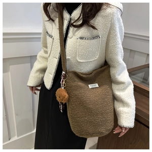 Close-up of brown plush bucket bag featuring a teddy bear charm and fashion label tag