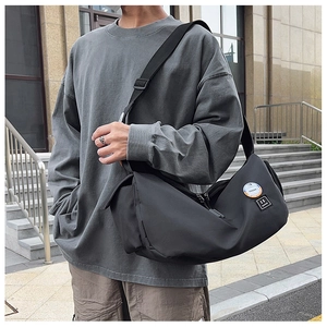 Detail of black nylon messenger bag with Trend patch worn by a male model in streetwear style