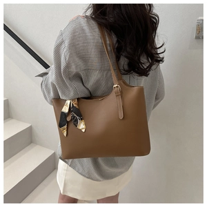 Detail of a brown tote bag featuring a decorative silk scarf and polished buckle strap