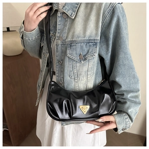 Detail of black pleated underarm bag featuring a golden triangular metal brand plaque