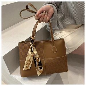 Detail of brown tote bag with checkered texture and silk scarf accessory on the handle