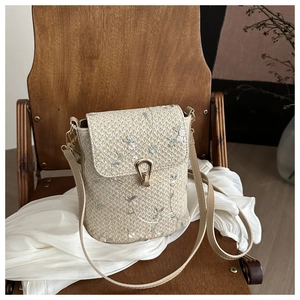 Detail of floral embroidery and gold metal clasp on woven straw crossbody handbag