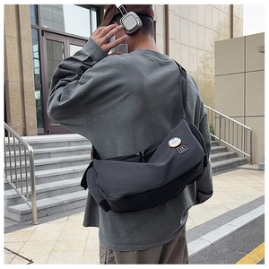 Outdoor view of a dark grey nylon messenger bag with adjustable strap and trend badges
