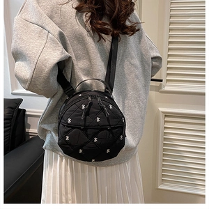 Close-up of black quilted round backpack with white bow patterns on a female model