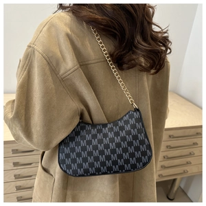 Detail of a black crescent underarm bag with M-pattern print and gold chain strap