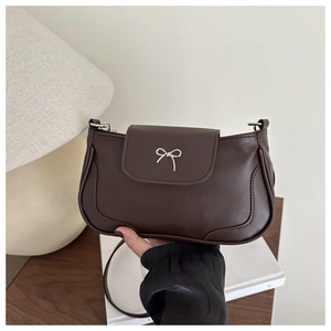 Detail of a chocolate brown underarm bag with a silver bow metal buckle and slim strap