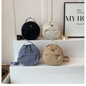 Multiple nylon round crossbody bags displayed on steps in black, beige, blue and khaki
