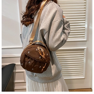 Detailed view of brown quilted round bag with small white embroidered bows and nylon strap