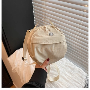 Detail of a beige nylon round bag showing adjustable straps and smooth dual zippers