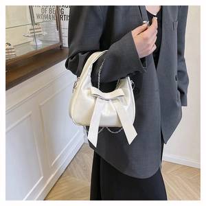 Close-up of cream bow-knot handbag with elegant silver chain detail in a cafe setting