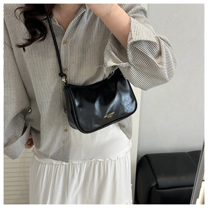 Detail of a shiny black faux leather crossbody bag with golden fashion lettering
