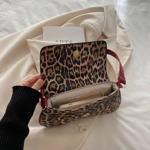 Large leopard print underarm bag with red shoulder strap and gold hardware on beige suit