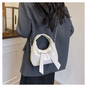 Model view showing the cream bow handbag worn with a grey blazer and black skirt