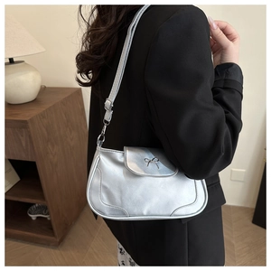 Detail of silver crossbody bag with metal bow buckle worn over the shoulder in a cozy room