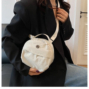 Detail of white nylon crossbody round bag showing wide strap and metallic buckle on model