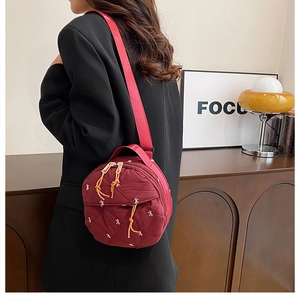 Detail of burgundy quilted round shoulder bag with white bow embroidery and red strap