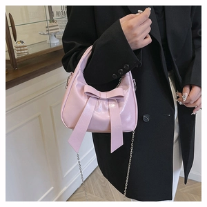 Detail of pink glossy handbag with large bow and silver chain on a black suit