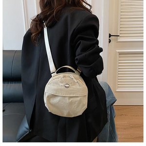 Detail of a beige round nylon crossbody bag showing the woven rope zipper and texture