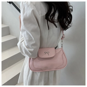 Detail of pink saddle bag with silver bow buckle worn over the shoulder by a model