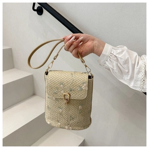 Dettaglio borsa in paglia beige con ricami floreali rosa e fibbia a ferro di cavallo dorata