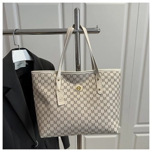 Close-up of white monogram tote bag with grey M pattern and gold circular logo hardware