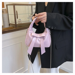 Close-up of pink crescent handbag featuring a large bow and silver chain strap