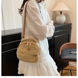 Detail of khaki nylon crossbody bag showing dual zipper pockets and top carry handle