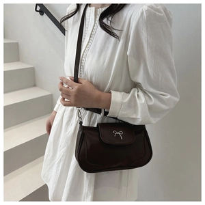 Detail of a dark brown leather crossbody bag with a small silver metal bow decoration