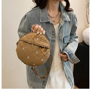 Macro view of brown quilted round bag with white bow embroidery and top handle