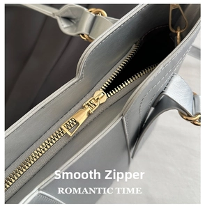 Close-up of smooth golden metal zipper and fine stitching on the grey leather bag