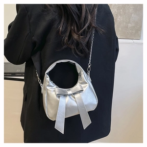 Detail of silver bow-knot crossbody bag with chain strap worn by a model