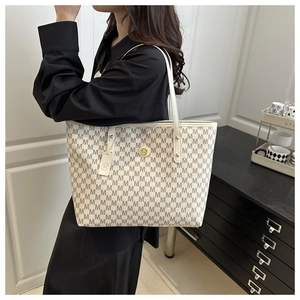 Detail of light beige tote bag featuring grey M pattern and gold metal logo charm