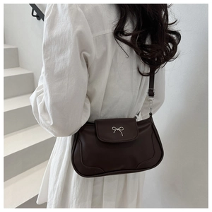 Detail of dark brown leather crossbody bag featuring silver metallic bow on a white stair