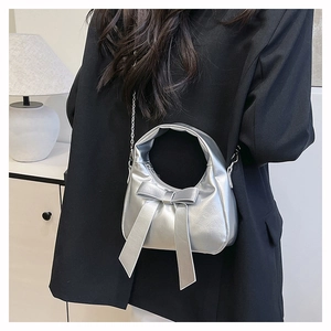 Close-up of a silver crescent hobo bag featuring a metallic bow and fine chain strap