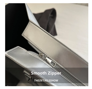 Detailed macro view of the smooth silver metal zipper on a shiny silver tote bag