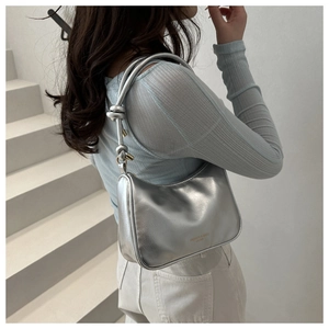 Close-up of metallic silver baguette bag featuring a stylish knotted shoulder strap detail