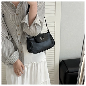 Detail of black leather half-moon bag with silver metal bow and slim shoulder strap