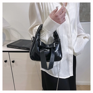 Detailed close-up of glossy black patent leather handbag with large bow and silver chain