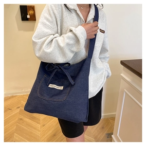 Detail view of large dark blue denim tote bag with front pocket and ribbon bow tie