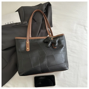 Détail du sac cabas noir avec anses marron et pendentif chien sur fond en tissu