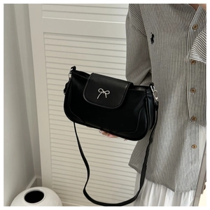 Detail of black crossbody bag featuring a silver metal bow buckle and matte leather texture