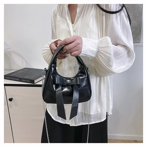 Detail of black glossy handbag with large bow decoration and silver metal chain strap