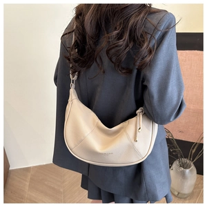 Detailed view of creamy beige pebbled leather crescent bag worn over a grey blazer