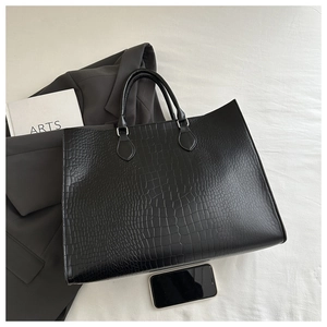 Detail of black crocodile embossed leather tote bag with smartphone for size reference