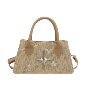 Woven straw crossbody bag with floral embroidery and silver star hardware on white background