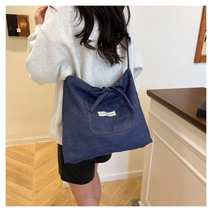 Detail of dark blue denim tote bag featuring a decorative bow and white fabric label pocket