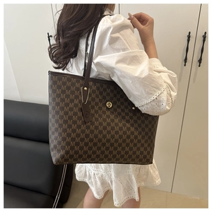 Detail of a brown tote bag with M letter prints and golden logo on a model's shoulder